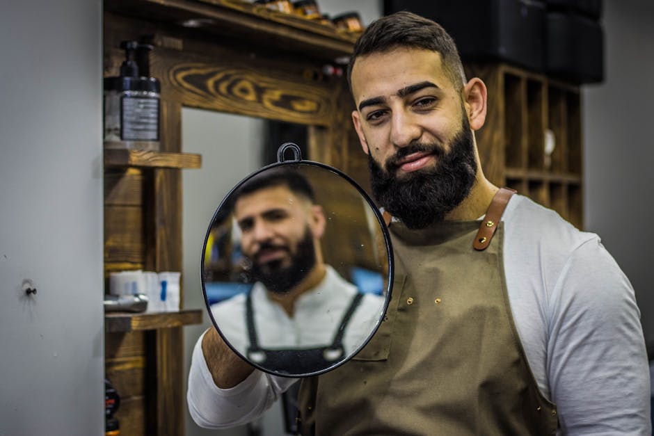 A bearded barber smiling while holding a mirror in a stylish barbershop. Ideal for lifestyle and grooming themes.