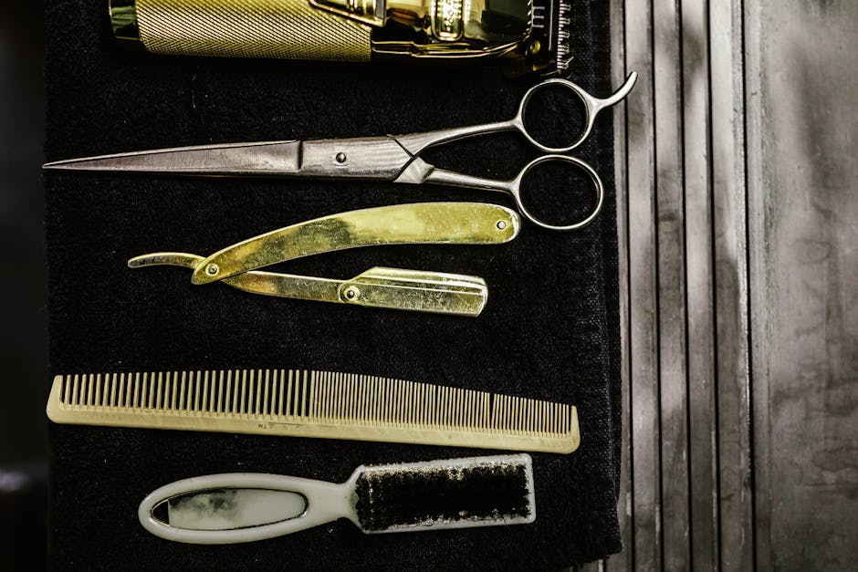 A set of vintage barber tools including scissors, razor, comb, and brush on a dark background.